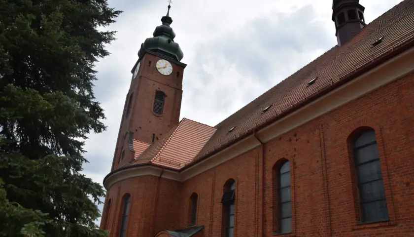 Ceglana wieża kościelna z zegarem i zielona choinka. Wygoda łączenia historii z naturą.