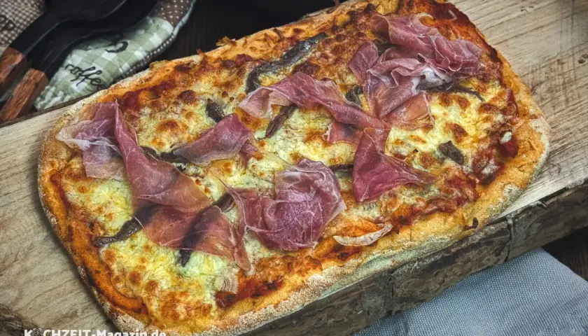 Frisch gebackene Pinsa mit zartem Schinken und geschmolzenem Käse auf rustikalem Holzbrett. Ein Genuss für jeden, der gerne Pinsa backen möchte.