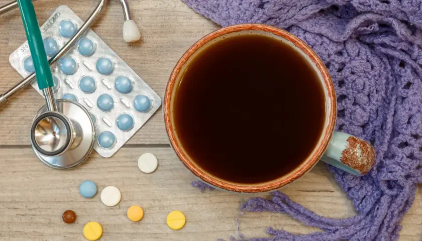 Tasse Kaffee, Stethoskop, Pillen und eine lila Decke. Vielleicht ist es Zeit für die **Selen Einnahme** und einen warmen Kaffee.
