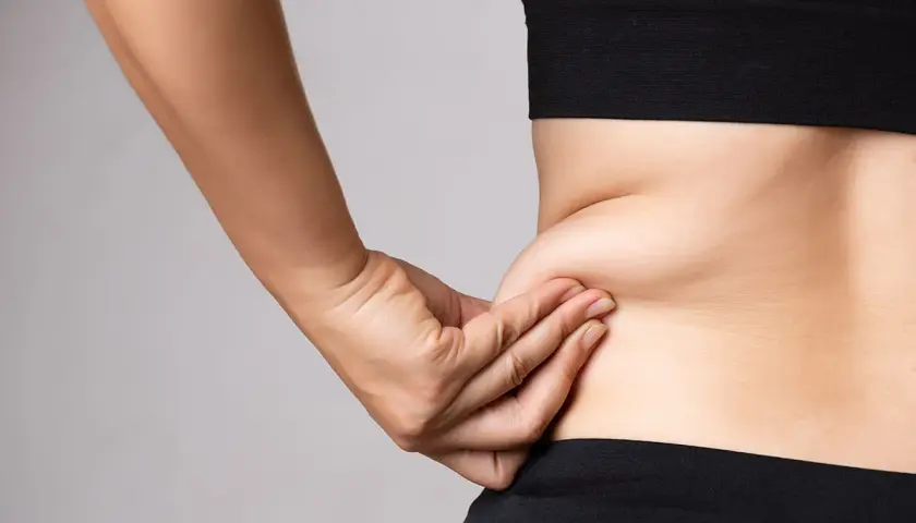 En hand som klämmer på fett på sidan av midjan, en vanlig indikation för coolsculpting.
