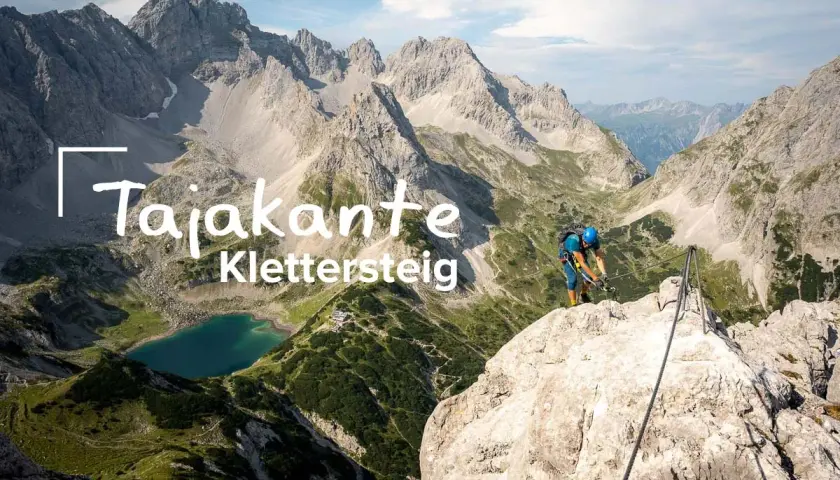 Ein Kletterer sichert sich am Tajakante Klettersteig mit Blick auf einen Bergsee.
