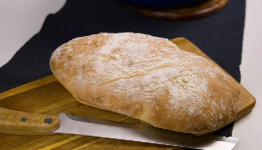 Nybakat bröd med en kniv på en skärbräda. Doften av nybakat bröd sprider sig i köket.