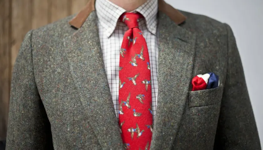 Elegancki garnitur z szarej szkockiej tkaniny wełnianej, czerwony krawat z kaczkami i chusteczka w barwach narodowych.