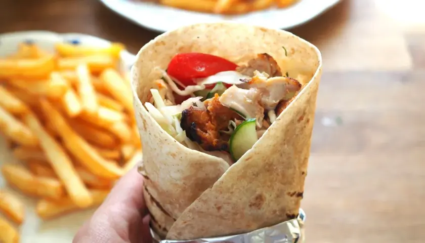 Domowy kebab w tortilli z kurczakiem, warzywami i frytkami w tle.