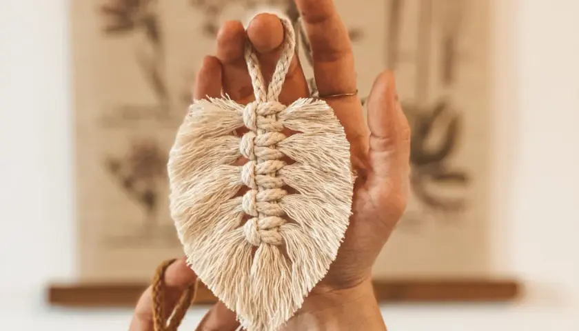 Eine Hand hält eine Makramee Feder. Die Anleitung für diese Feder ist einfach und das Ergebnis ist ein schönes Deko-Objekt.