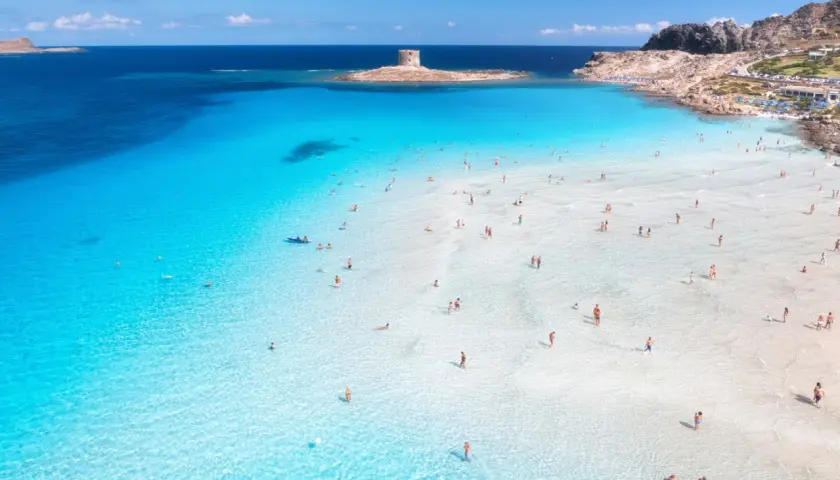 Türkises Wasser und ein alter Turm auf Sardinien. Menschen genießen das flache, klare Meer an einem sonnigen Tag.