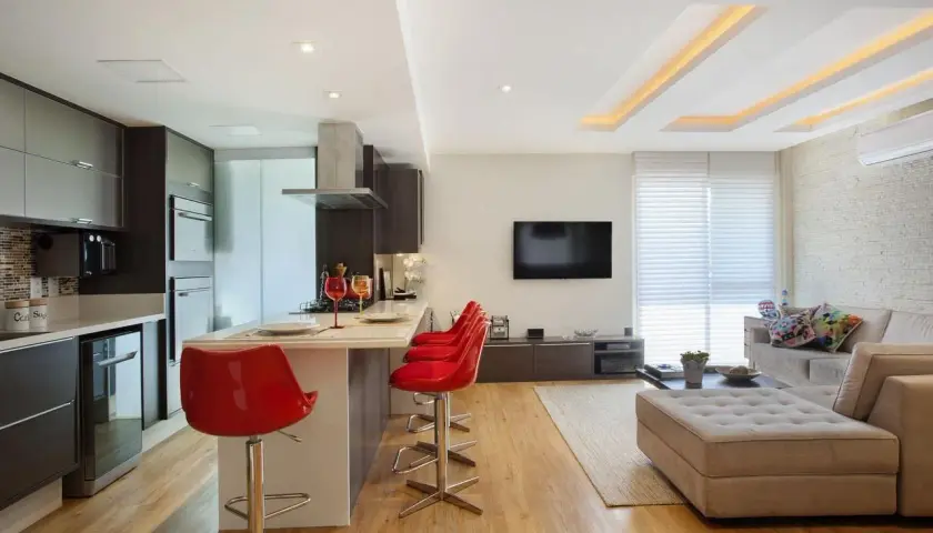Cucina moderna con isola e sgabelli rossi, soggiorno con divano e TV. Il soffitto in cartongesso design crea un'atmosfera accogliente.