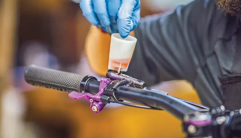 Gloved hand pours fluid into a bike's brake lever, a step in learning how to bleed hydraulic lines.