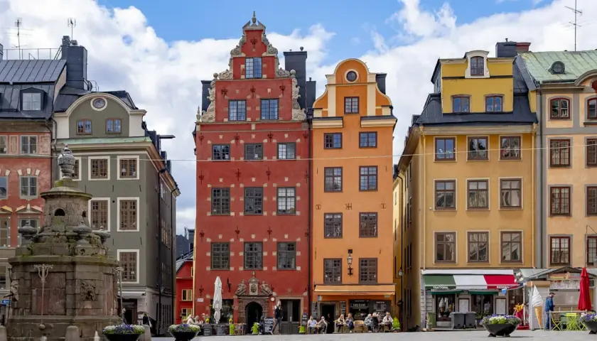 Färgglada hus på Stortorget, Stockholm sommar. En fontän står framför de gamla byggnaderna.
