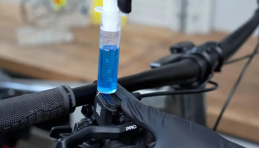 A syringe filled with blue fluid is used to bleed the brakes on a bicycle.