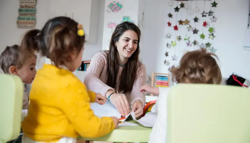 Eine Kinderpflegerin lächelt, während sie mit Kindern bastelt. Sie fragt sich, wie viel verdient man als Kinderpflegerin?