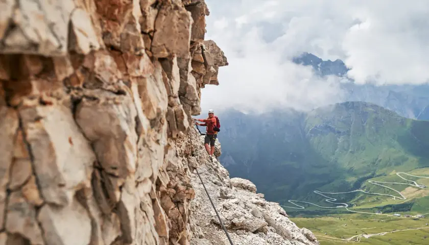 Wspinacz na via ferrata w Dolomitach, z widokiem na kręte drogi i zielone doliny.