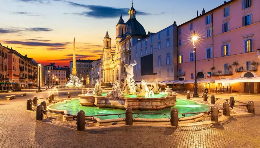 Fontaine de la piazza Navona illuminée au crépuscule, avec l'obélisque et l'église en arrière-plan.