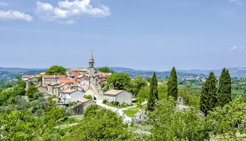 Kleine kroatische Stadt Hum mit Kirchturm, umgeben von grünen Hügeln und Bäumen.