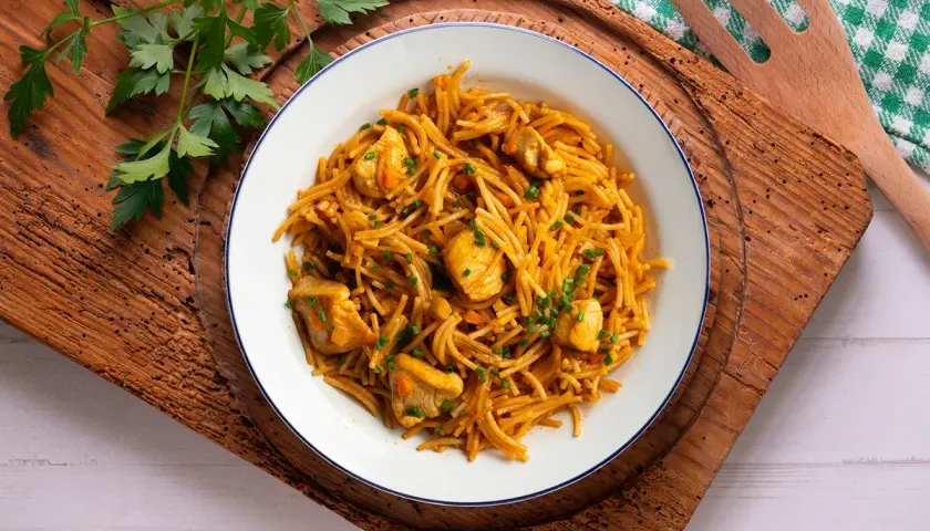 Delicioso plato de fideuà de pollo, con fideos finos y trozos de pollo tierno, decorado con perejil fresco.