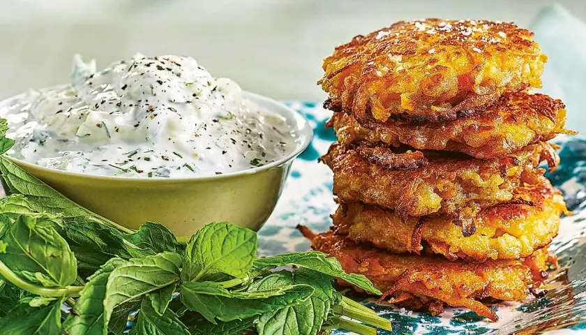 En stapel gyllene halloumi morotsbiffar serveras med en krämig yoghurtsås och färsk mynta.