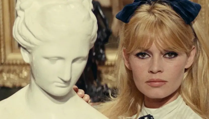 Brigitte Bardot z niebieską kokardką we włosach, obok antycznej rzeźby. Ikona lat 60 muzyka i stylu.