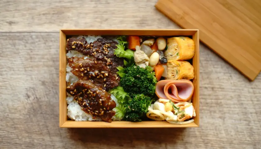 A delicious Japanese convenience store bento box filled with rice, teriyaki beef, broccoli, tamagoyaki, ham, and salad.