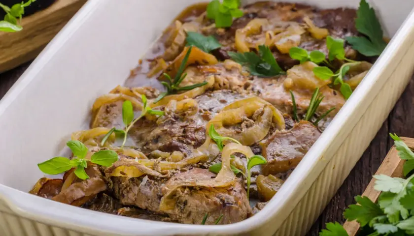 Pyszny kotlet husarski duszony z cebulą i ziołami, podany w białej brytfannie.