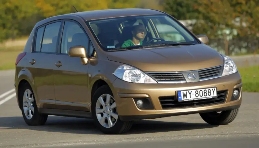 Złoty Nissan Tiida z mężczyzną za kierownicą jedzie po drodze.