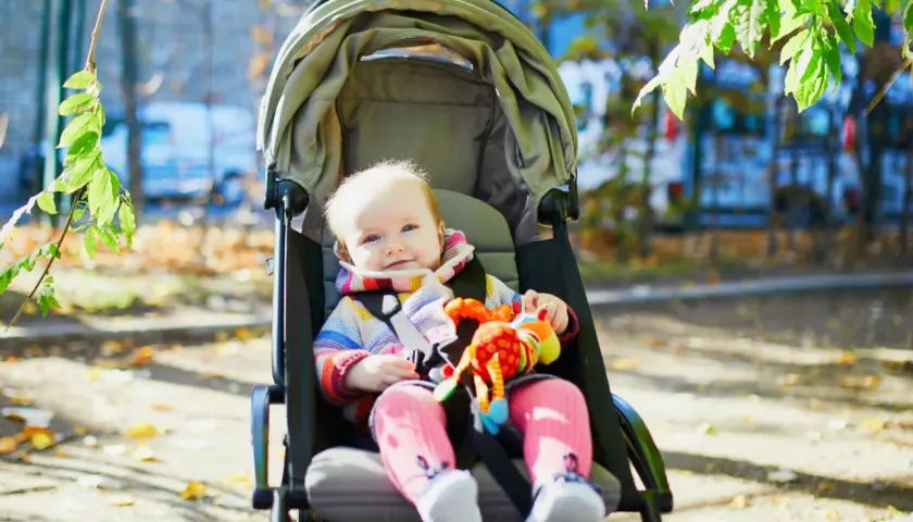 Uśmiechnięte dziecko w wózku spacerowym, gotowe na jesienne wycieczki. Czas na zmianę gondoli na spacerówkę, gdy maluch zaczyna siedzieć.
