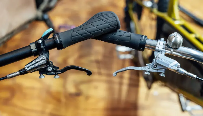 Close-up of bicycle handlebars featuring black Ergon grips and silver and black Hope e4 brakes, ready for any trail.