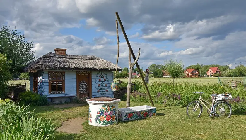 Kolorowy dom malarek w Zalipiu, z kwiecistymi zdobieniami, studnią i rowerem.