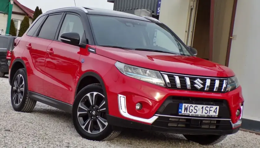 Czerwony Suzuki Vitara Hybrid z czarnym dachem, zaparkowany na żwirowej nawierzchni.