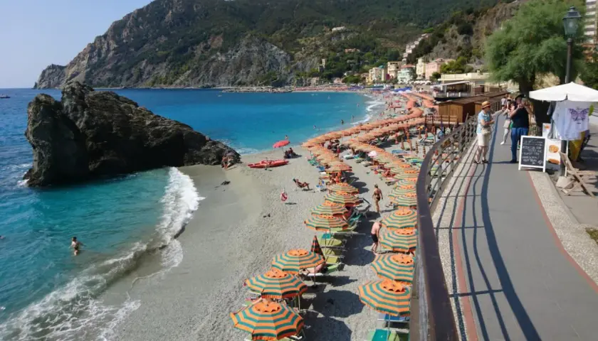 Plage animée à Moneglia, Italie, avec des parasols rayés, des baigneurs dans la mer turquoise et des collines verdoyantes en arrière-plan.