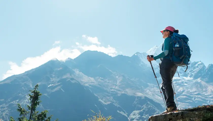 Kobieta z plecakiem i kijkami trekkingowymi podziwia majestatyczne góry. To jej wycieczka na Mount Everest, pełna wyzwań i piękna.