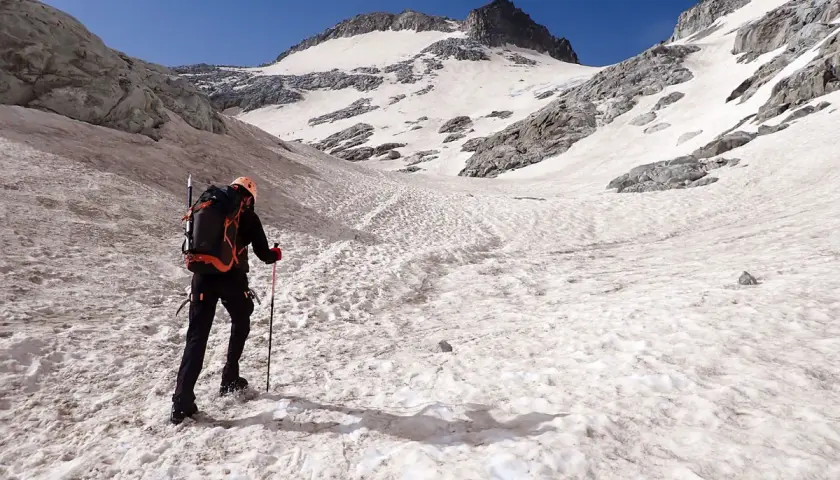 Alpinista asciende por una ladera nevada hacia el pico Aneto, con el cielo azul brillante.