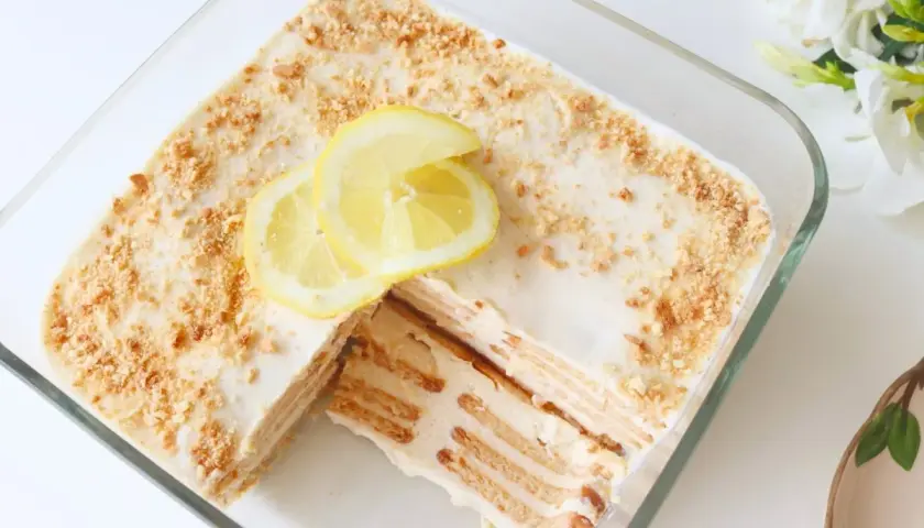 Deliciosa carlota de limón en un recipiente de vidrio, decorada con rodajas de limón y migas de galleta.