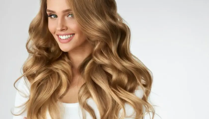 Mujer sonriente con cabello ondulado color miel rubio, que cae sobre sus hombros.