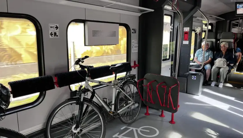 Wygodna podróż pociągiem z rowerem. W wagonie są specjalne miejsca na rower, a obok siedzą pasażerowie.