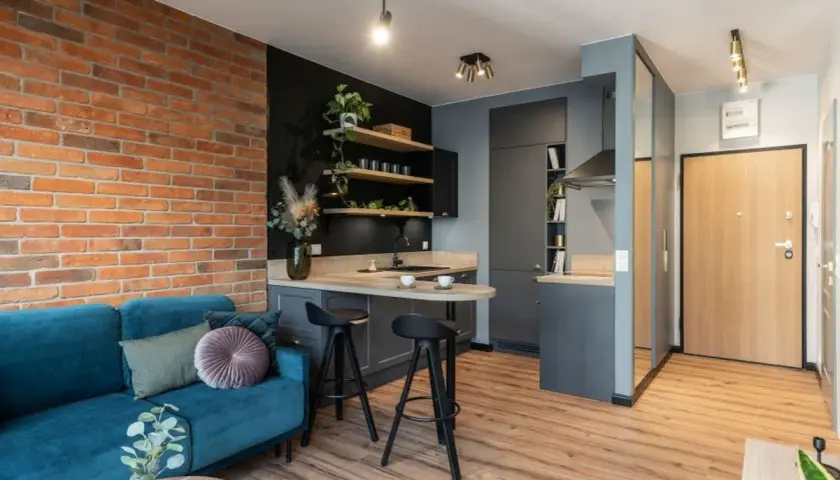 Nowoczesne mieszkanie 35m2 plan: salon z turkusową kanapą, kuchnia z wyspą i ceglaną ścianą.