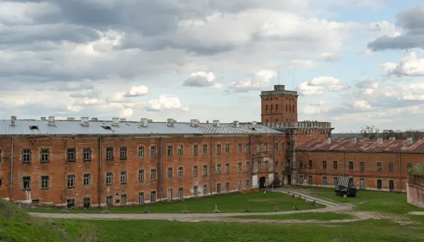 Dawny fort wojskowy w okolicach Warszawy, z ceglanymi budynkami i wieżą.