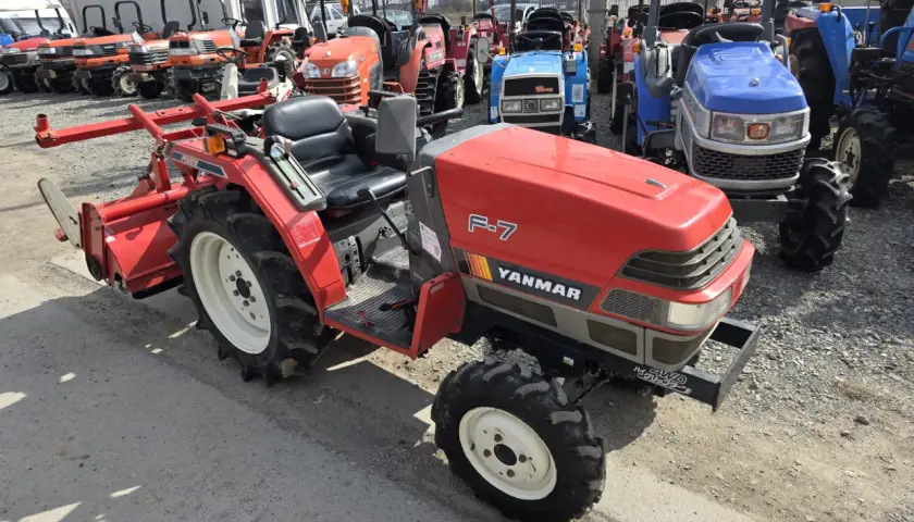 Czerwony ciągnik Yanmar F-7 z osprzętem, obok inne maszyny. Zastanawiasz się, ile oleju do skrzyni biegów?