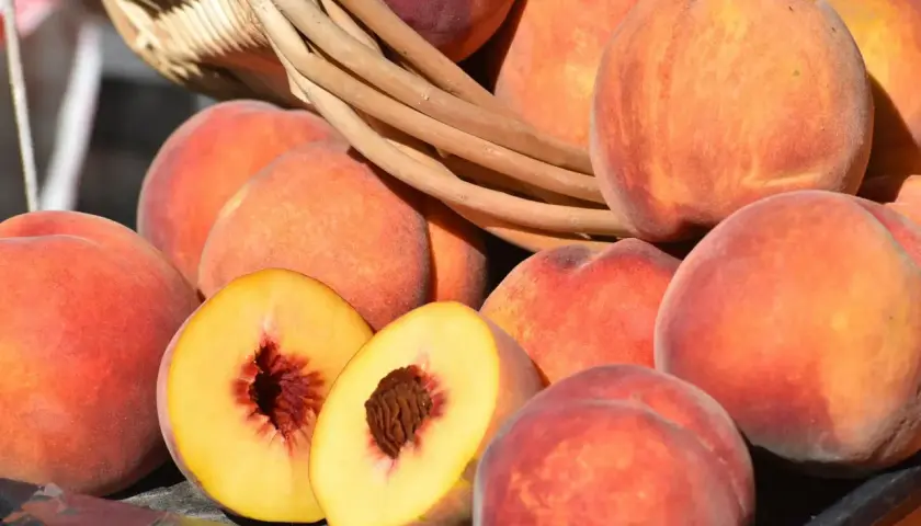 Frische Pfirsiche und Nektarinen lagern in einem Korb. Eine Frucht ist aufgeschnitten und zeigt das saftige Innere.