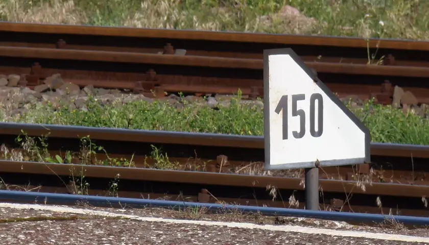 Biały trójkątny wskaźnik w11 z czarną liczbą 150 obok torów kolejowych.