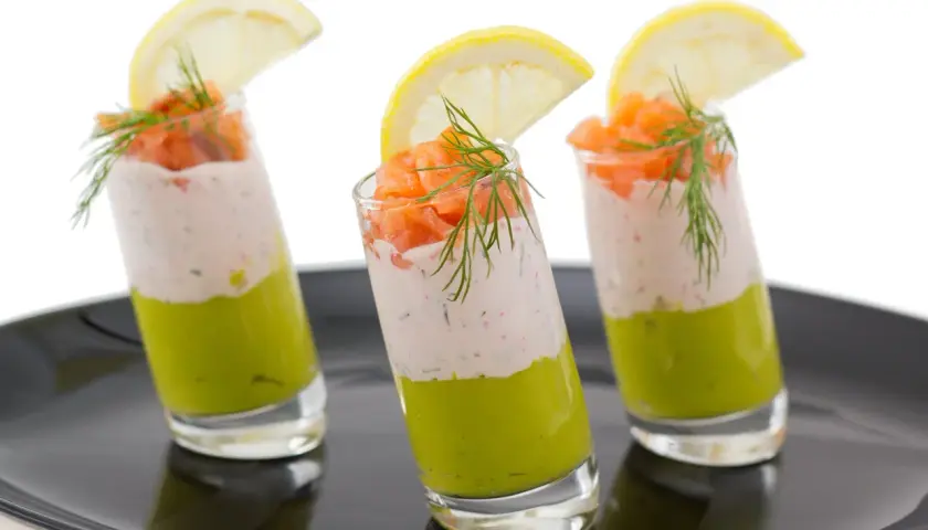 Trois verrines charcuterie : avocat, crème et saumon fumé, garnies d'aneth et d'une tranche de citron.