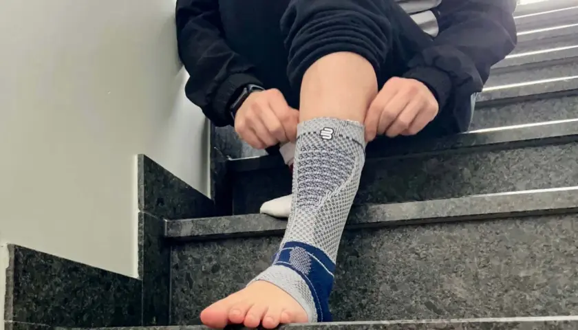 Person zieht eine Bandage am Fuß an, die bei einem Achillessehnenriss Schuh-Schmerzen helfen soll.
