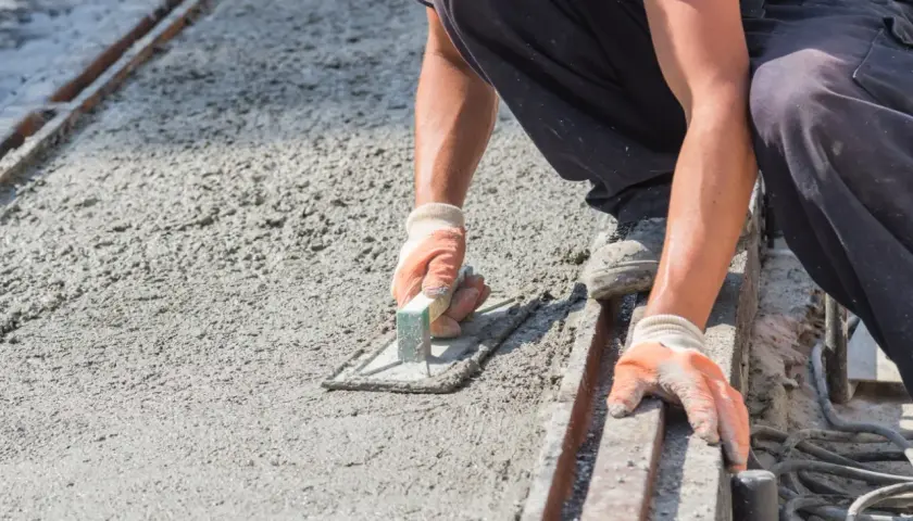 Pracownik w rękawiczkach wygładza świeży beton, dbając o właściwe proporcje i równość powierzchni.