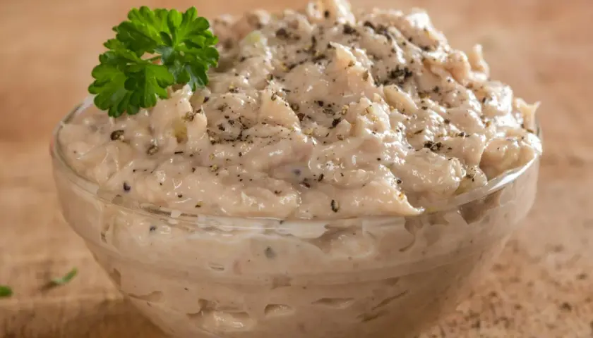 Pyszna pasta z tuńczyka, doprawiona pieprzem i udekorowana natką pietruszki, w szklanej miseczce na drewnianym tle.