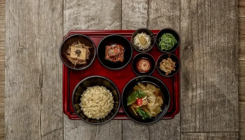 Korean temple food: eine Schale Reis, Tofu, Kimchi und verschiedene Gemüsebeilagen auf einem roten Tablett.