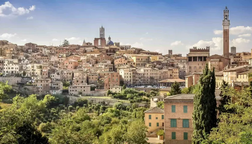 A panoramic view of Siena's historic skyline, a beautiful destination on the journey from Lucca to Siena. The Torre del Mangia tower stands tall amidst terracotta rooftops.