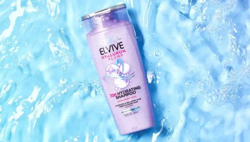 Botella de champú Elvive Hyaluron Plump sobre fondo azul con burbujas, ideal para pelo seco.