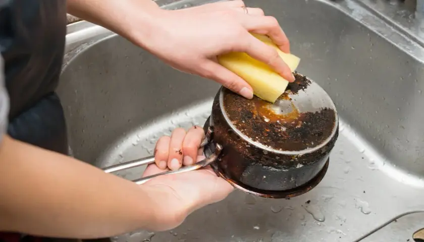 Nettoyage d'une casserole brûlée avec une éponge. Le bicarbonate de soude sera utile pour cette tâche difficile.