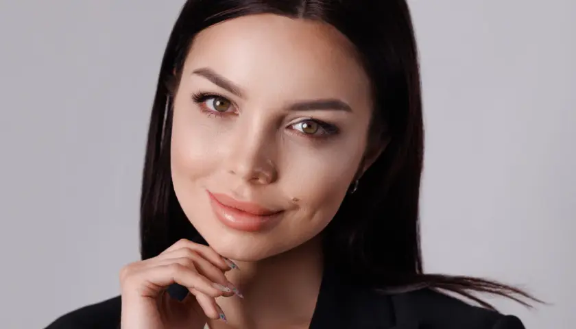 Elegancka kobieta w czarnej marynarce, opierająca podbródek na dłoni, pozuje w studiu.