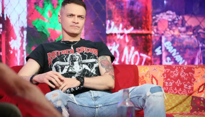 Nocny kochanek wokalista w czarnej koszulce z Britney Spears, siedzi na kanapie w podartych jeansach.