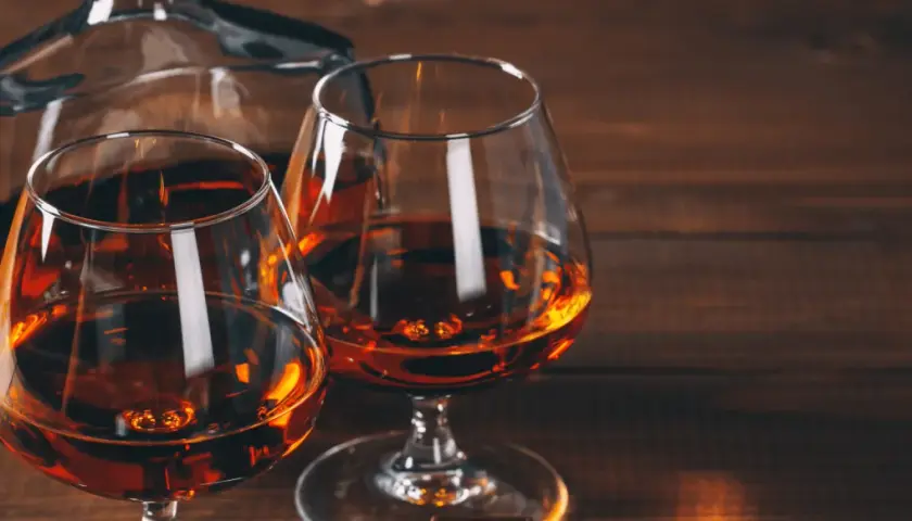 Dwa kieliszki z bursztynowym koniakiem i karafka na drewnianym stole. Idealny wieczór z brandy.